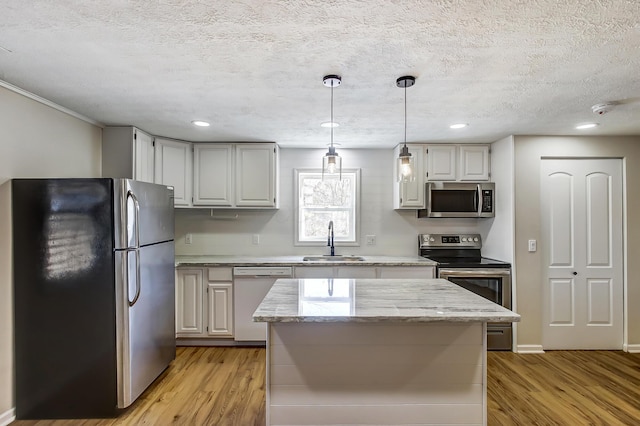 kitchen with a sink, hanging light fixtures, light wood finished floors, and stainless steel appliances