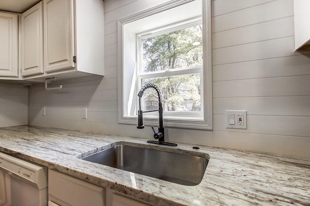 kitchen featuring dishwasher, light stone countertops, wood walls, and a sink