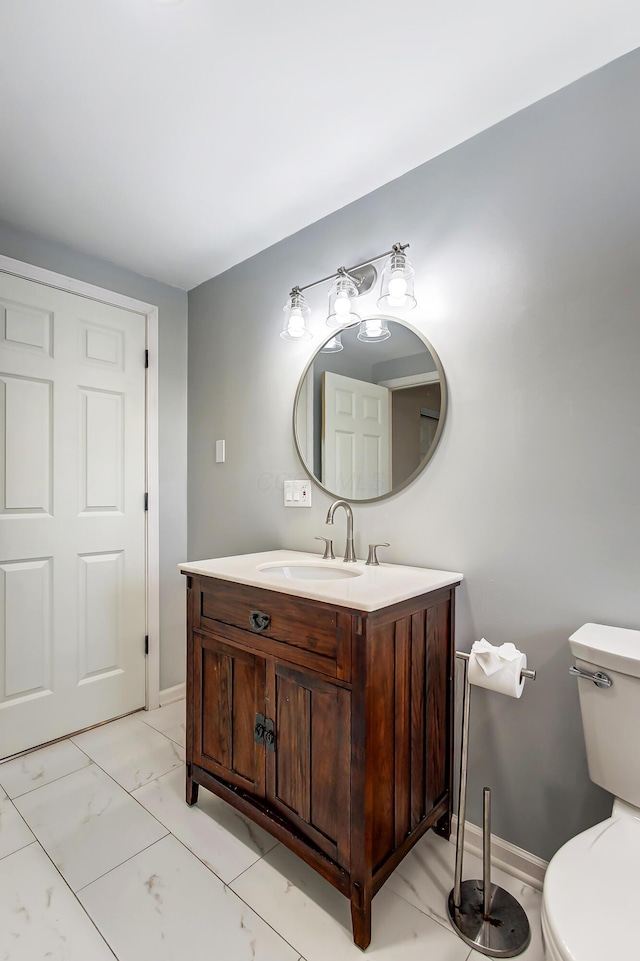 half bath featuring marble finish floor, toilet, vanity, and baseboards