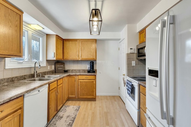 kitchen featuring light wood-type flooring, decorative backsplash, brown cabinets, white appliances, and a sink