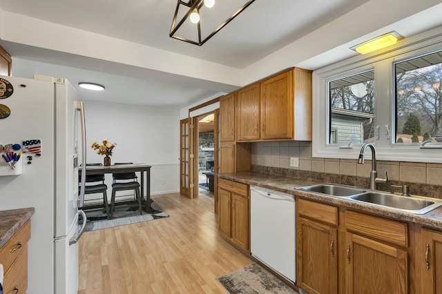 kitchen with decorative backsplash, white appliances, light wood-style floors, and a sink