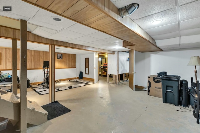 finished below grade area featuring wood walls, a paneled ceiling, and baseboards