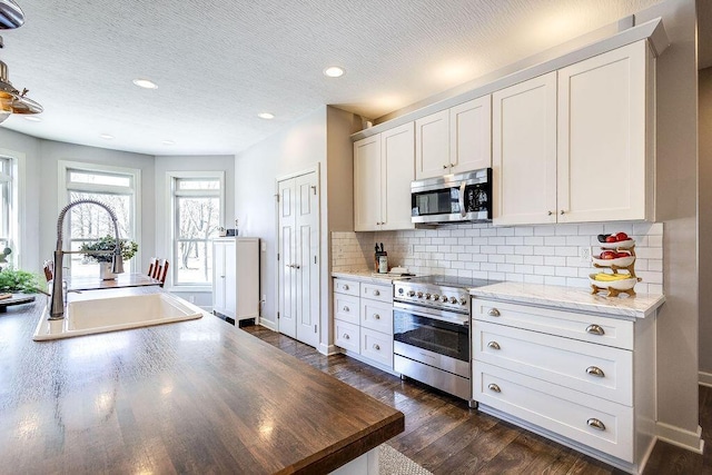 kitchen with dark wood-type flooring, a sink, backsplash, a textured ceiling, and stainless steel appliances