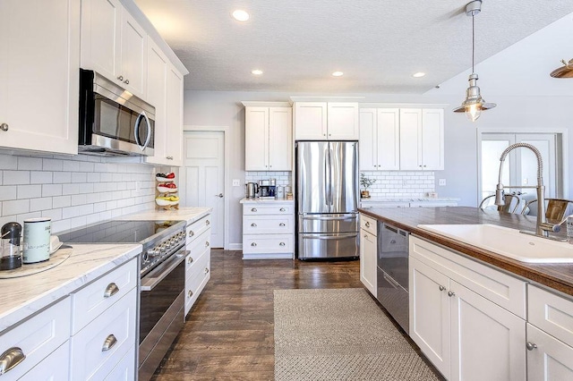 kitchen featuring dark wood finished floors, stainless steel appliances, hanging light fixtures, white cabinetry, and a sink