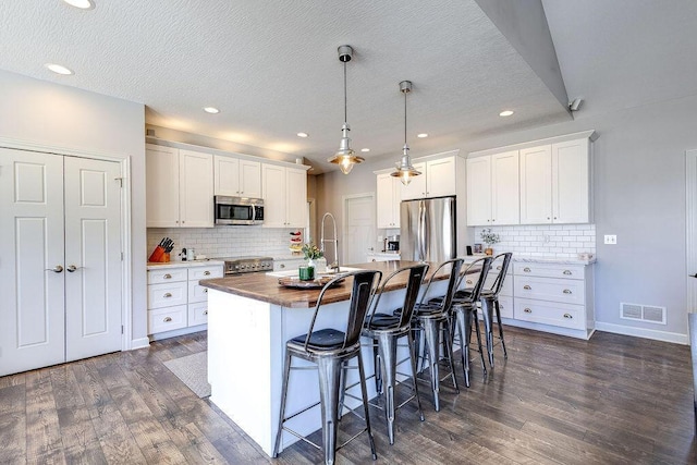 kitchen featuring visible vents, a kitchen island with sink, dark wood-style floors, stainless steel appliances, and a breakfast bar area