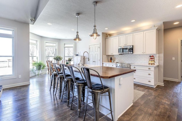 kitchen featuring a kitchen island with sink, a sink, stainless steel microwave, decorative backsplash, and wooden counters