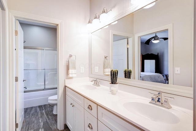 bathroom with a sink, bath / shower combo with glass door, toilet, and double vanity