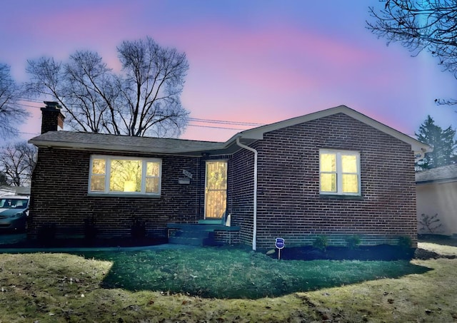 view of front of property featuring brick siding, a lawn, and a chimney