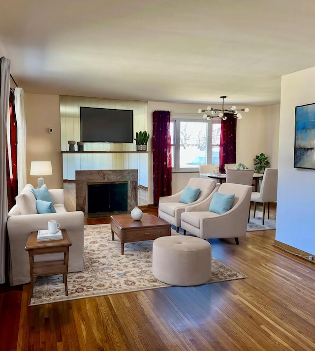 living area with a high end fireplace, an inviting chandelier, and wood finished floors