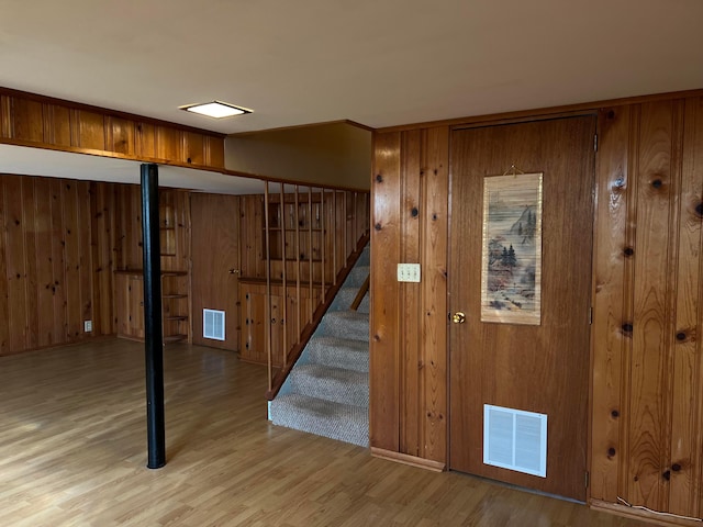 finished basement with visible vents, stairway, wooden walls, and wood finished floors