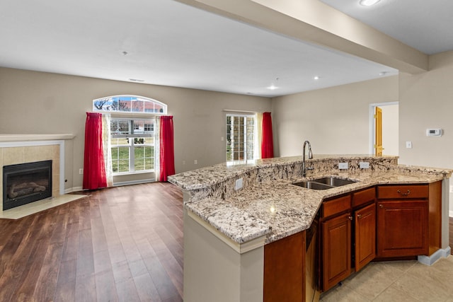 kitchen with light stone countertops, light wood-style flooring, a sink, a tiled fireplace, and open floor plan