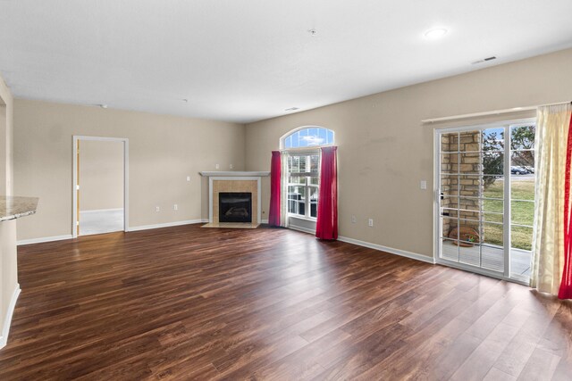unfurnished living room featuring baseboards, dark wood-type flooring, and a tile fireplace