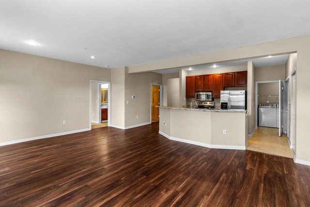 kitchen featuring baseboards, light stone countertops, stainless steel appliances, wood finished floors, and washer / clothes dryer