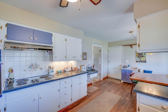 kitchen featuring light wood-style flooring, under cabinet range hood, tasteful backsplash, stainless steel electric cooktop, and dark countertops