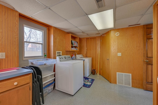 clothes washing area featuring laundry area, wooden walls, washing machine and dryer, and visible vents