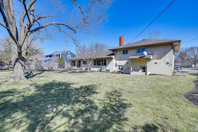 rear view of property featuring stucco siding, a yard, fence, and a chimney