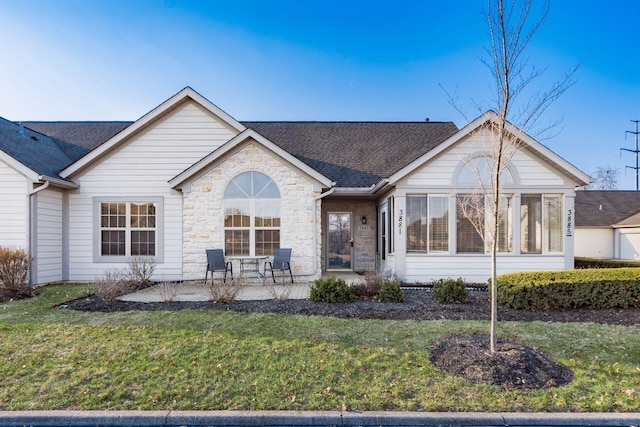 ranch-style home featuring a patio area, stone siding, a shingled roof, and a front yard