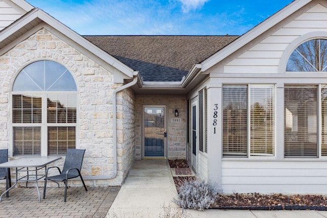 doorway to property with stone siding, roof with shingles, and a patio