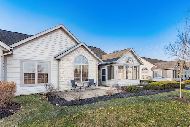 back of house featuring stone siding, a patio, a sunroom, a yard, and a shingled roof