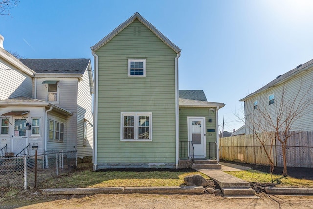 rear view of house featuring entry steps, roof with shingles, and fence