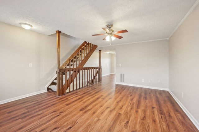 empty room with wood finished floors, baseboards, visible vents, a textured ceiling, and crown molding