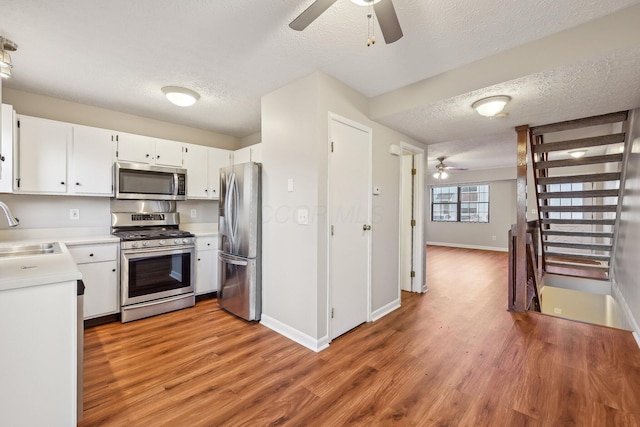 kitchen with light wood finished floors, a sink, light countertops, appliances with stainless steel finishes, and a textured ceiling