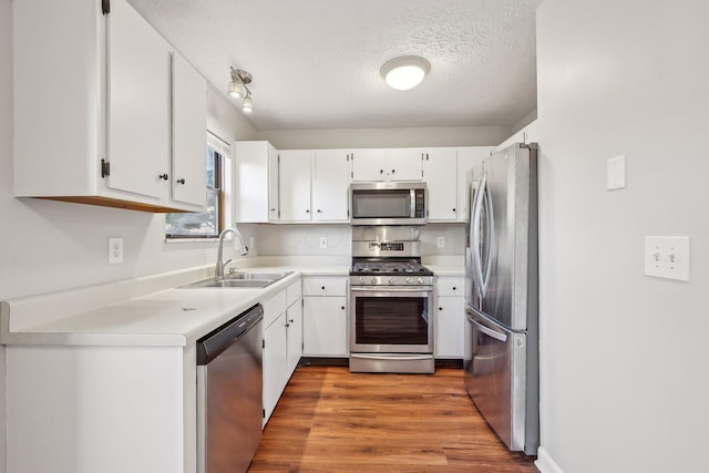 kitchen with stainless steel appliances, wood finished floors, a textured ceiling, white cabinetry, and a sink