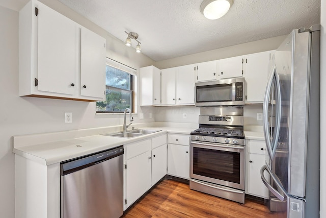 kitchen with white cabinets, appliances with stainless steel finishes, wood finished floors, and a sink