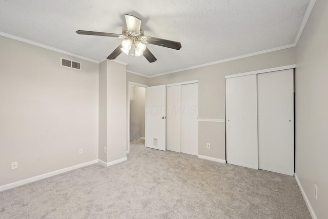 unfurnished bedroom featuring visible vents, multiple closets, carpet floors, and ornamental molding