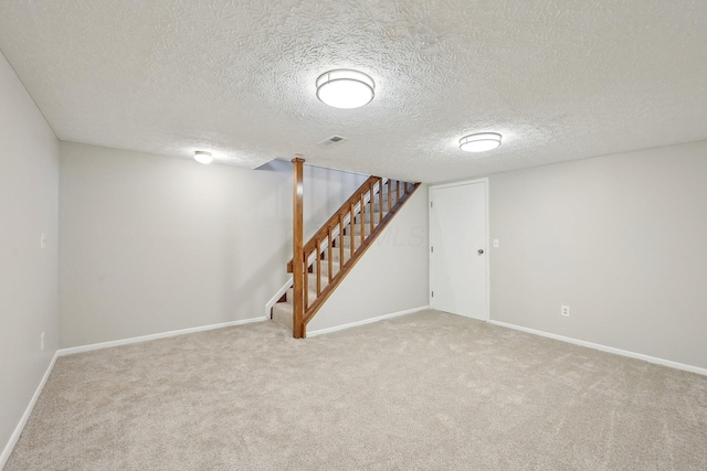 finished below grade area featuring visible vents, baseboards, stairway, carpet flooring, and a textured ceiling