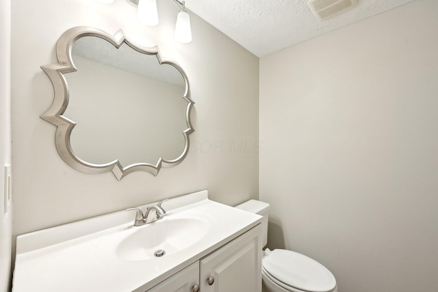 half bathroom featuring vanity, toilet, visible vents, and a textured ceiling