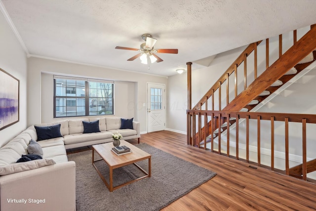 living room featuring crown molding, baseboards, stairs, wood finished floors, and a textured ceiling