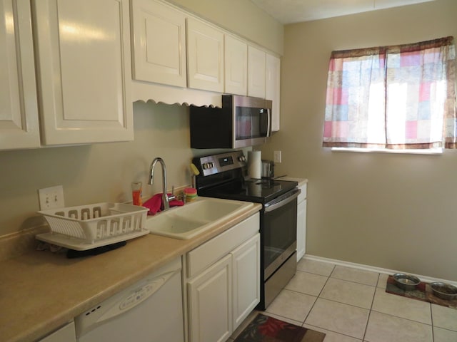 kitchen with light tile patterned flooring, a sink, light countertops, white cabinets, and appliances with stainless steel finishes