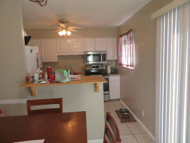 kitchen with ceiling fan, light countertops, light tile patterned floors, appliances with stainless steel finishes, and white cabinets