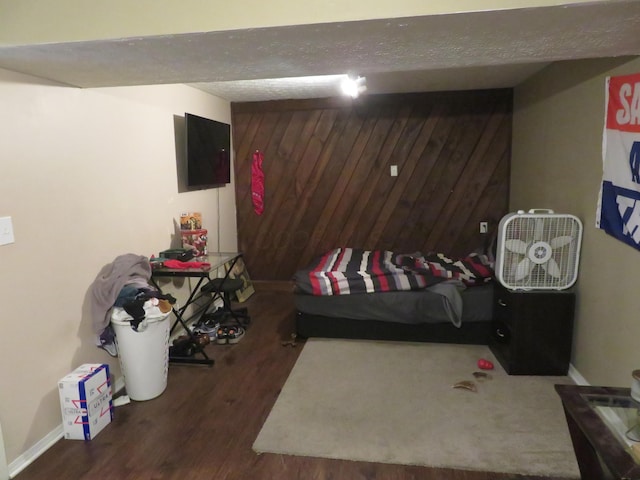 finished basement with wooden walls, a textured ceiling, baseboards, and wood finished floors