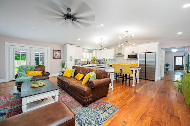 living area featuring light wood-type flooring, french doors, a healthy amount of sunlight, and an inviting chandelier