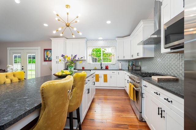 kitchen with a sink, stainless steel appliances, white cabinets, and wall chimney range hood