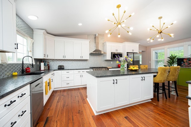 kitchen featuring a sink, a kitchen island, stainless steel appliances, wall chimney range hood, and vaulted ceiling