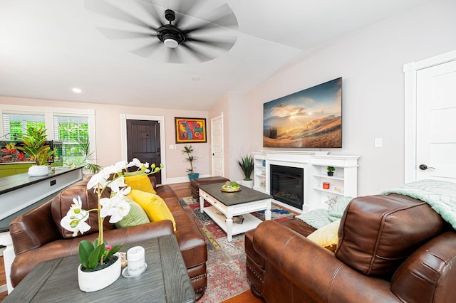 living room featuring ceiling fan, baseboards, a glass covered fireplace, and vaulted ceiling