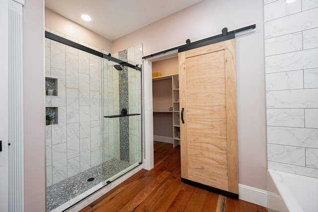 bathroom with a shower stall, a walk in closet, baseboards, a tub to relax in, and wood-type flooring