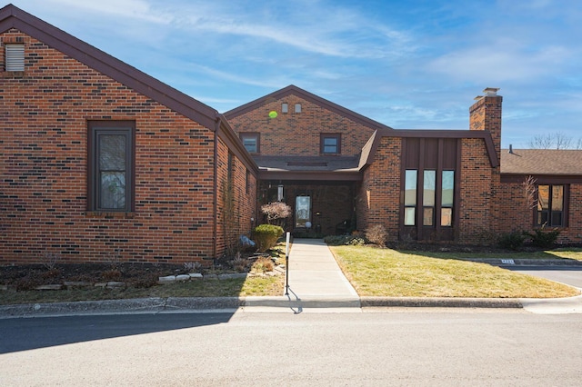 view of front of property featuring brick siding, a chimney, and a front lawn