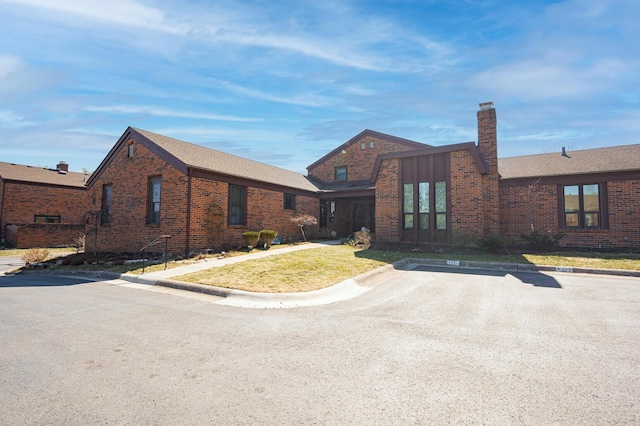 view of front of property featuring brick siding, a chimney, a front lawn, and uncovered parking