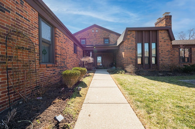 doorway to property featuring a lawn, brick siding, and a chimney