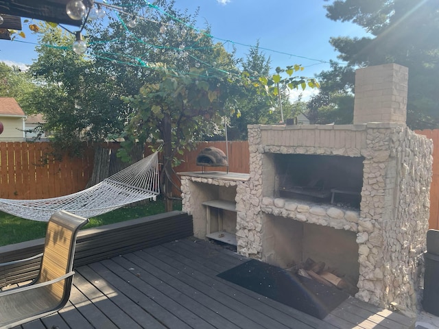 wooden deck with an outdoor stone fireplace and fence