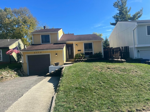 tri-level home with aphalt driveway, an attached garage, a front lawn, and fence