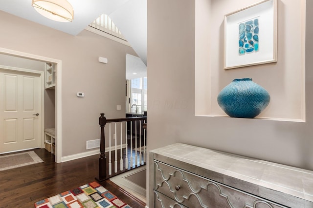 corridor with dark wood-type flooring, an upstairs landing, visible vents, and baseboards