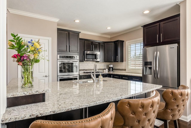 kitchen with tasteful backsplash, appliances with stainless steel finishes, a kitchen breakfast bar, and ornamental molding