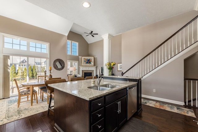 kitchen with dark wood-type flooring, a center island with sink, dishwasher, a fireplace, and a sink