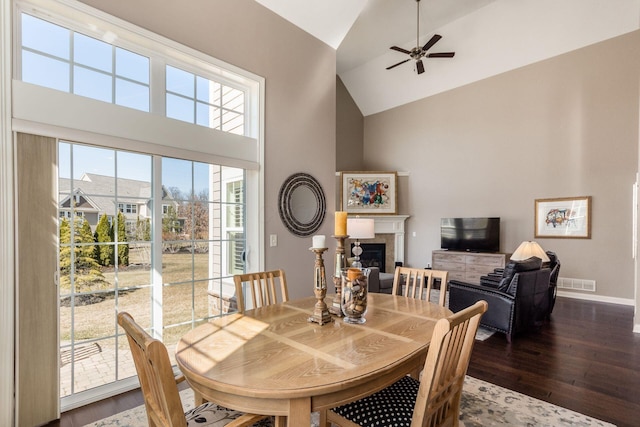 dining area with wood finished floors, visible vents, high vaulted ceiling, ceiling fan, and a glass covered fireplace