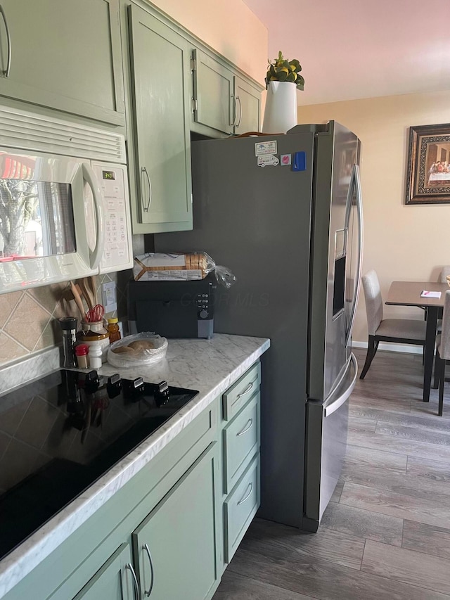 kitchen with white microwave, backsplash, dark wood finished floors, light countertops, and green cabinetry